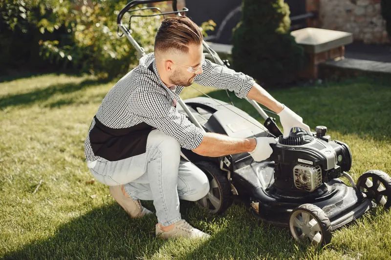 Man preparing lawn mower for garden work on a sunny day outdoors