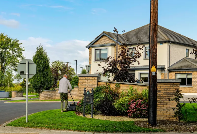 A man mowing the lawn outside a modern suburban home with a lush garden and clear blue sky