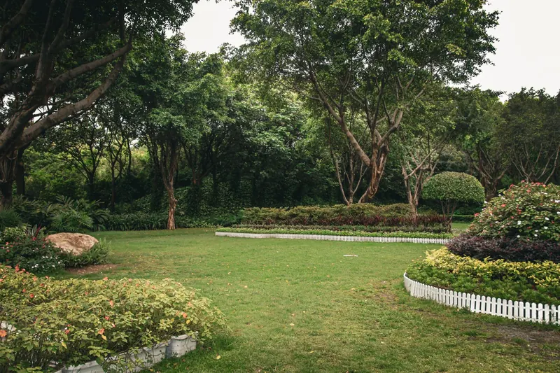 A serene garden with trees, flower beds, and manicured lawns surrounded by greenery