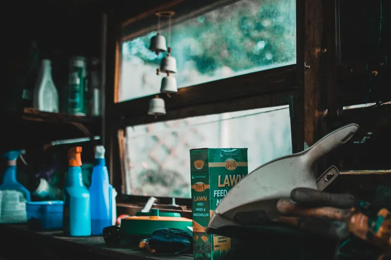 A cozy indoor garden shed scene with tools and lawn supplies by a window