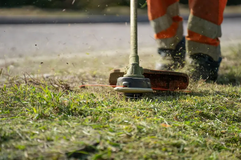Close-up of a person trimming grass with a power tool outdoors