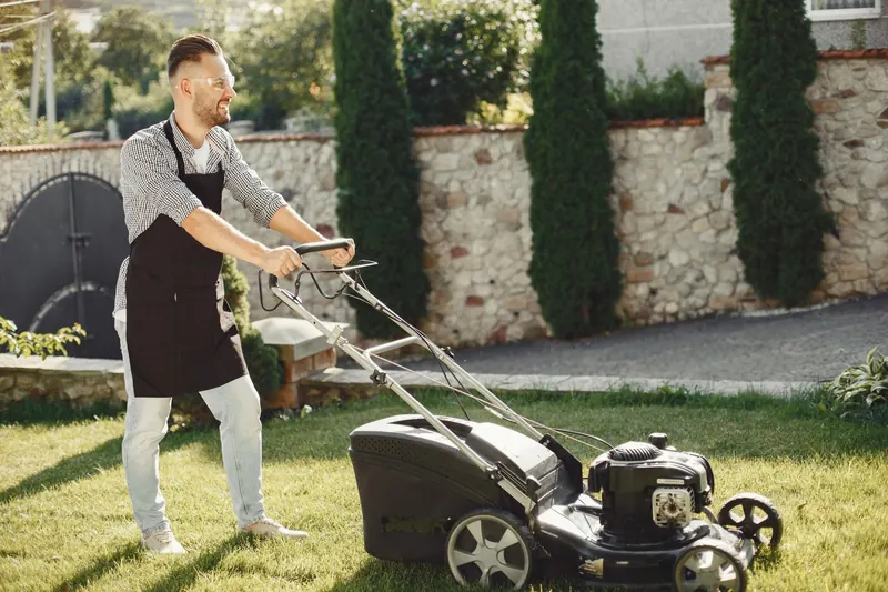 A man using a lawn mower to trim grass in a sunny outdoor garden