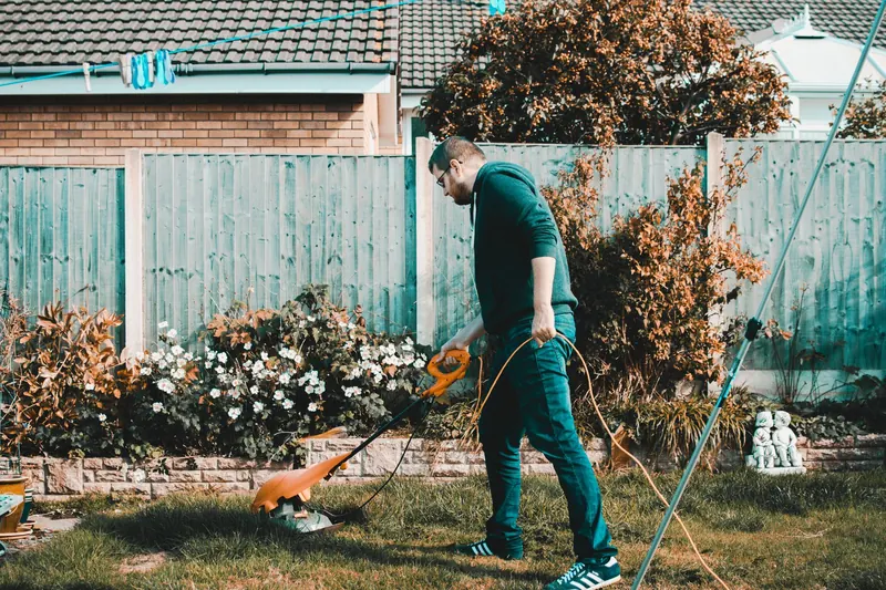 A man using an electric mower in a garden on a sunny day, capturing outdoor chores and gardening vibes