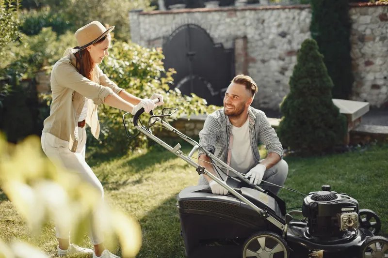 A cheerful couple working together in a garden with a lawn mower