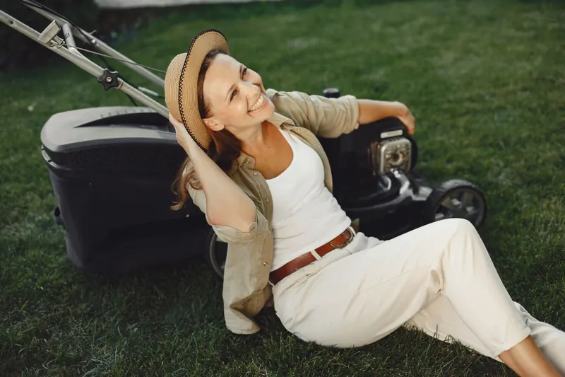 A cheerful woman relaxes on a lawn with a mower, exuding a serene and content vibe