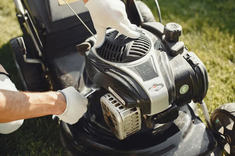 Hands in gloves adjusting a lawn mower outdoors, perfect for gardening themes