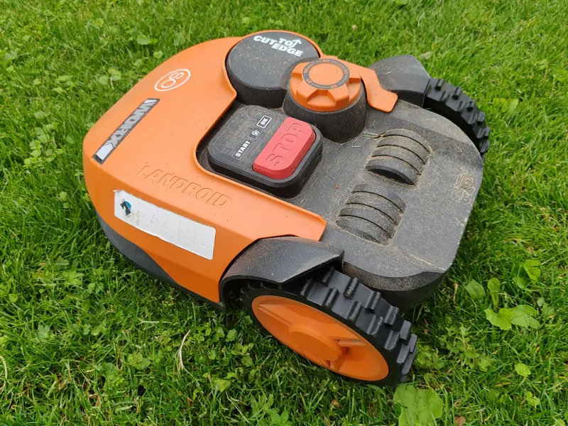 A modern robotic lawn mower in vibrant orange resting on a green lawn, ready for automated mowing tasks